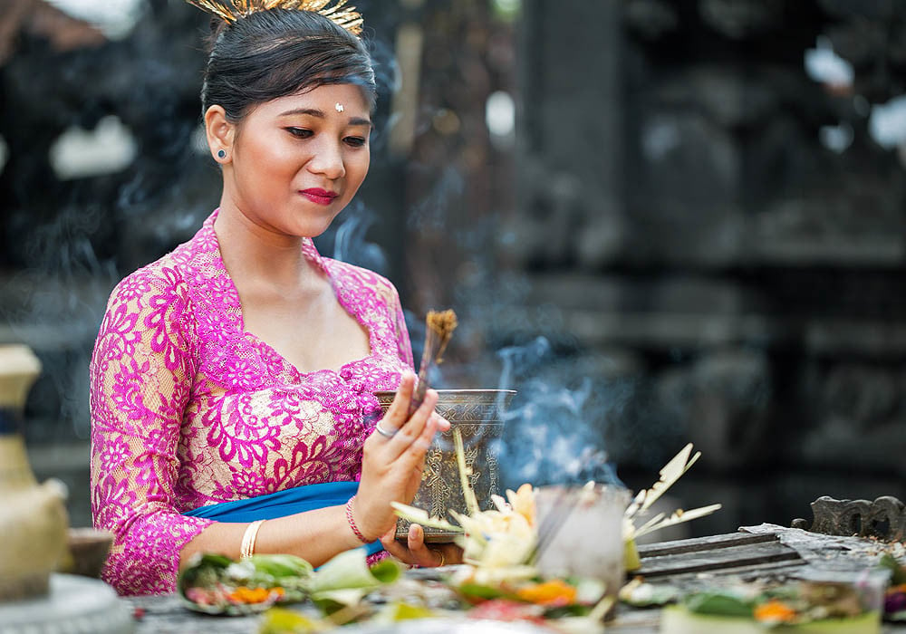 A Balinese Hindu woman blesses her offerings with tirta - holy spring water - and burning incense