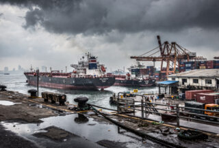Bustling port in Mumbai with oil tankers and cargo ships under overcast sky