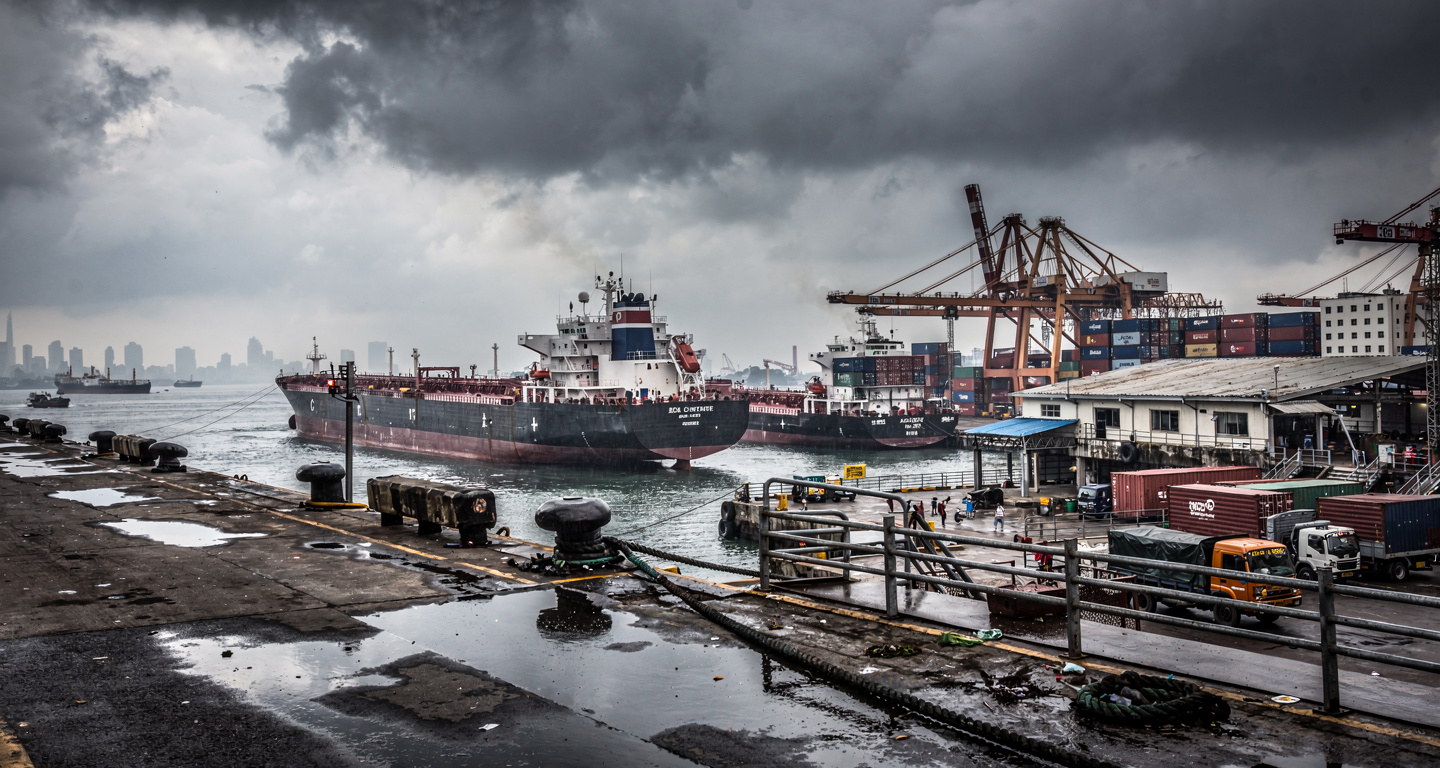 Bustling port in Mumbai with oil tankers and cargo ships under overcast sky
