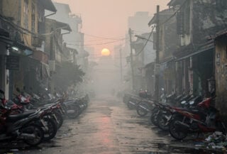 Hanoi street shrouded in smog with parked motorbikes and scooters, heavy air pollution