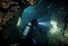 Underwater cave diver navigating a narrow, dark, flooded tunnel in Laos
