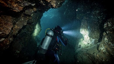 Underwater cave diver navigating a narrow, dark, flooded tunnel in Laos