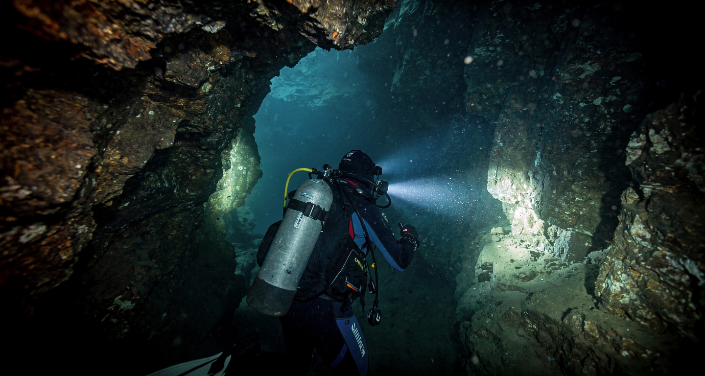 Underwater cave diver navigating a narrow, dark, flooded tunnel in Laos