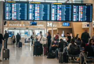 Airport departure board showing flight cancellations, Gulf hub terminal, travellers with luggage