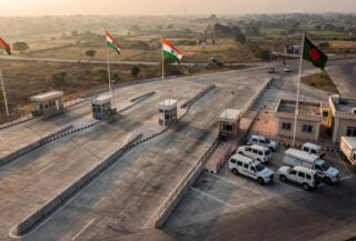 Border checkpoint between India and Bangladesh with concrete barriers and flags at dawn