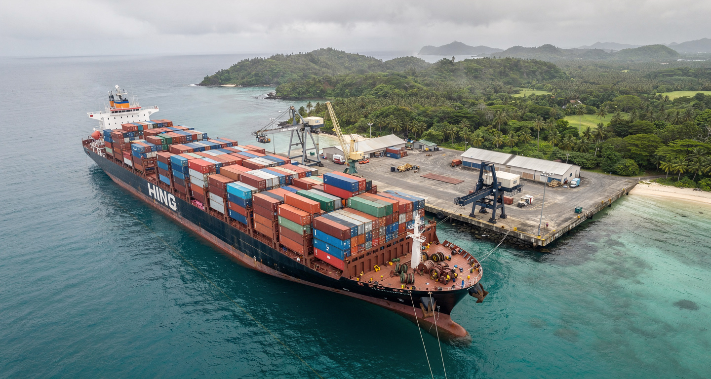 Container ship at small Pacific island port with stacked cargo containers