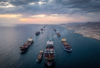 Container ships transiting Strait of Hormuz at dawn, narrow waterway between Iran and Gulf states