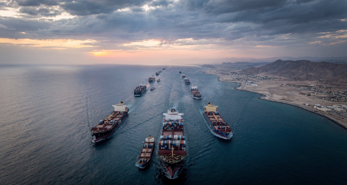 Container ships transiting Strait of Hormuz at dawn, narrow waterway between Iran and Gulf states