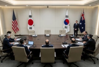 Diplomatic conference table with flags of US, Japan, South Korea, and Australia