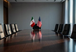 Empty negotiation table in Swiss conference room with Iranian and US flags