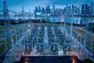 High-voltage electrical grid transmission lines at dusk with Singapore skyline