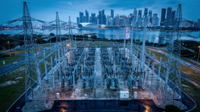 High-voltage electrical grid transmission lines at dusk with Singapore skyline