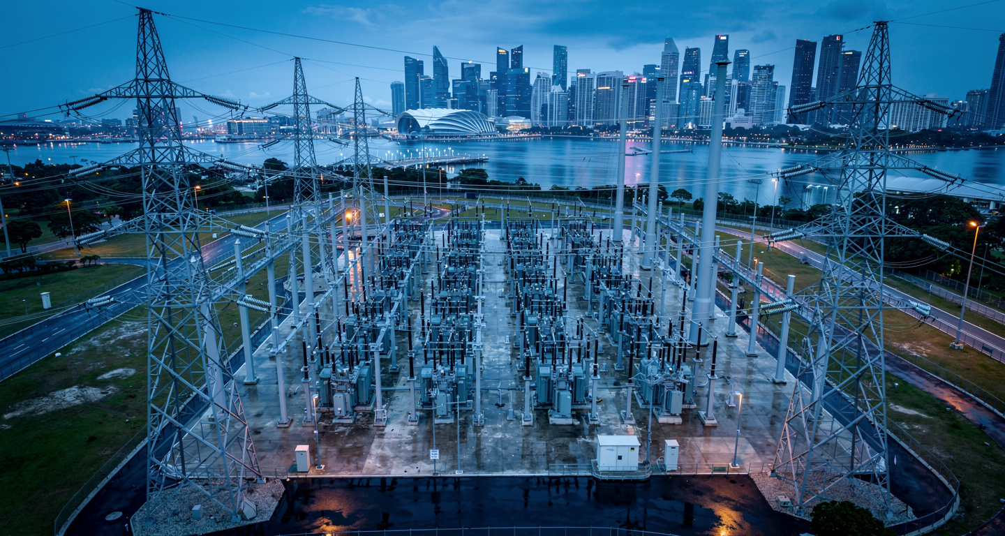 High-voltage electrical grid transmission lines at dusk with Singapore skyline