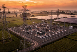 High-voltage transmission lines and substations at dusk, rural Southeast Asia, with solar panels visible