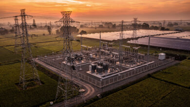 High-voltage transmission lines and substations at dusk, rural Southeast Asia, with solar panels visible