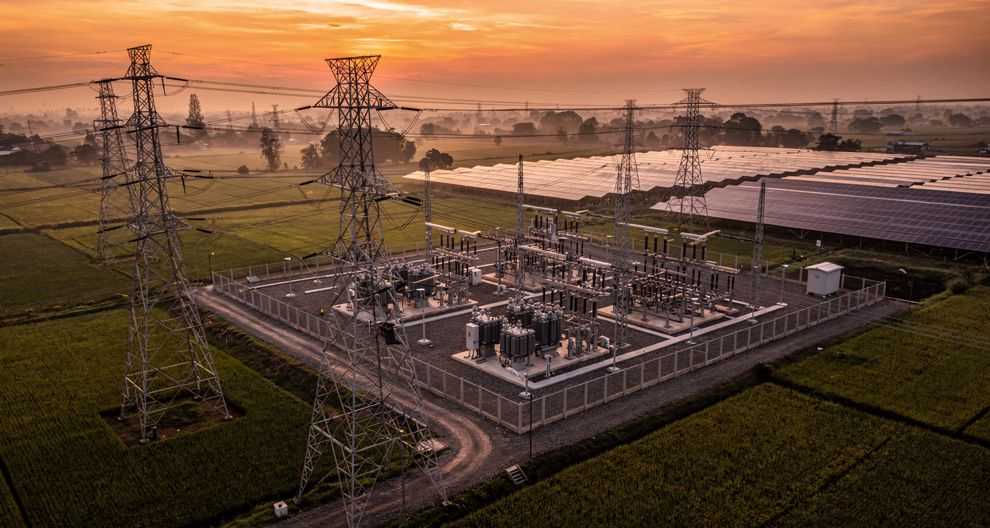 High-voltage transmission lines and substations at dusk, rural Southeast Asia, with solar panels visible