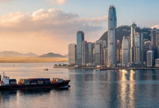 Hong Kong financial district skyline at dusk overlooking Victoria Harbour with cargo vessel