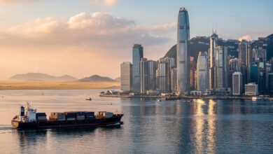 Hong Kong financial district skyline at dusk overlooking Victoria Harbour with cargo vessel