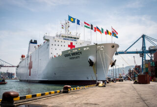 Hospital ship USNS Mercy docked at Southeast Asian port with flags and medical infrastructure visible