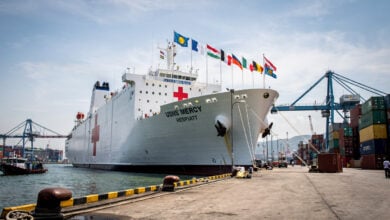 Hospital ship USNS Mercy docked at Southeast Asian port with flags and medical infrastructure visible