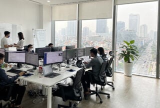 Modern tech office interior in Hanoi with engineers at workstations and city skyline