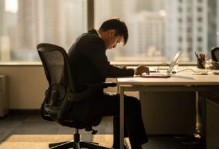 Office worker at desk, face turned away, modern corporate workspace with afternoon light