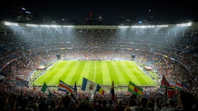 Packed football stadium at night with fans holding Asian national flags under dramatic lighting