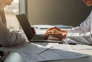 Student at desk with exam papers and laptop, Middle East office setting