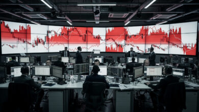 Trading floor with red market indices and oil price charts displayed on screens
