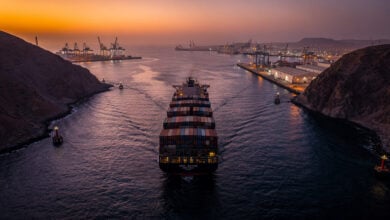 Container ship transiting narrow Red Sea strait with port infrastructure visible