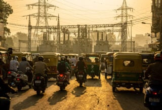 Delhi street traffic with three-wheelers and two-wheelers, power lines overhead