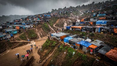 Hillside refugee camp in Cox's Bazar during monsoon rains, steep terrain with makeshift shelters