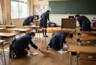 Japanese students cleaning classroom with brooms during school day