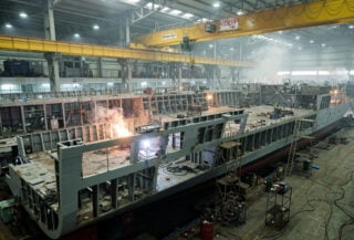Modular frigate hull sections under assembly in Indian shipyard with industrial cranes
