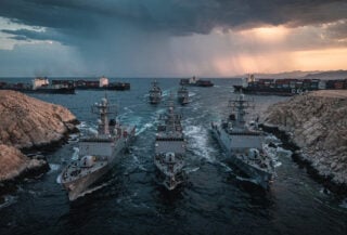 Naval vessels in Strait of Hormuz at dawn with container ships, dramatic storm clouds
