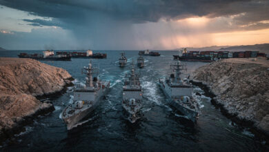 Naval vessels in Strait of Hormuz at dawn with container ships, dramatic storm clouds