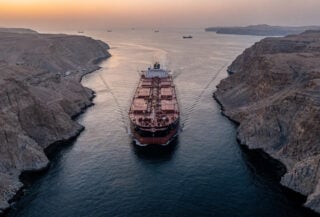 Oil tanker transiting Strait of Hormuz at dawn, narrow waterway between Iran and Oman