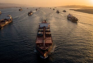 Oil tanker navigating Strait of Hormuz at dusk with container ships in narrow waterway