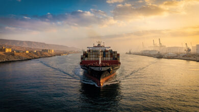 Tanker ship transiting narrow Strait of Hormuz at dawn between Iran and Oman