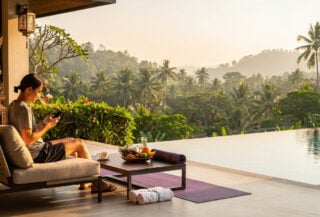 Young traveler planning trip on phone at luxury resort terrace, tropical landscape, Bali