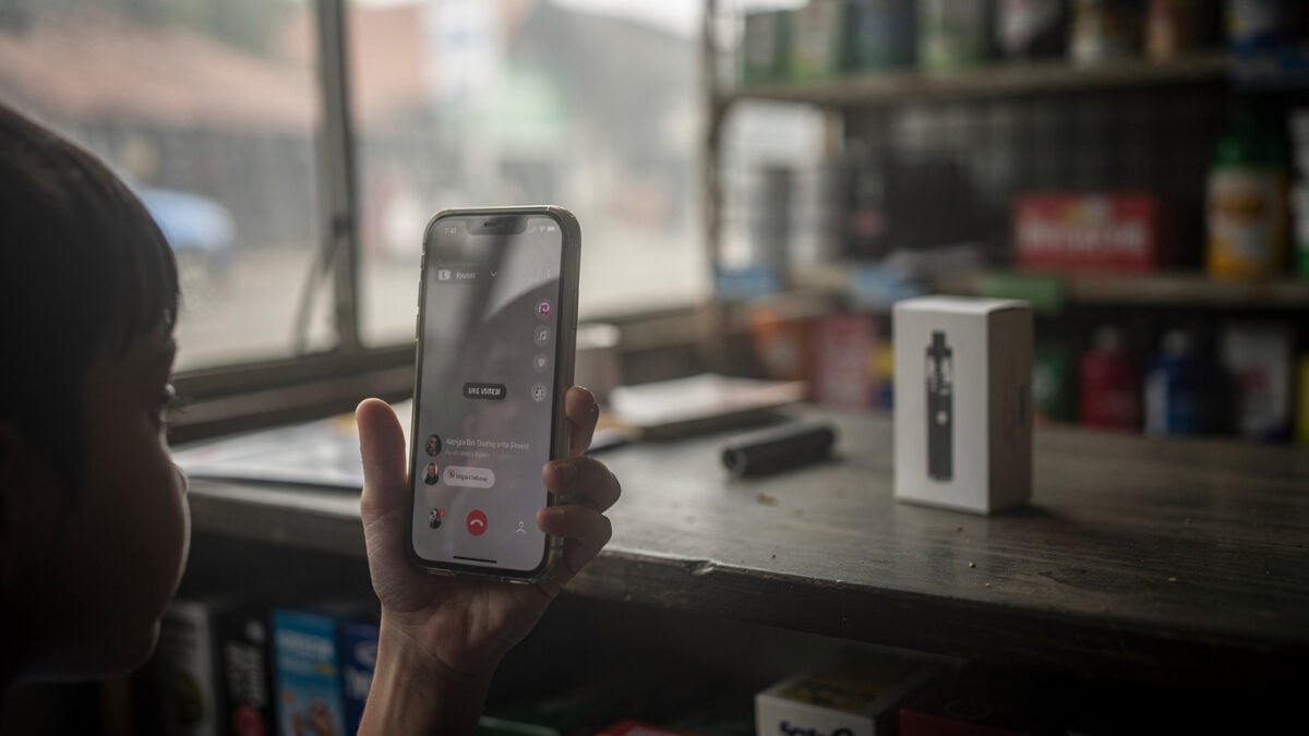 Child's hand with smartphone livestream interface, vaping shop counter background, Jakarta