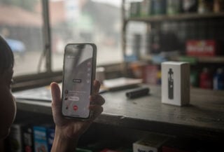 Child's hand with smartphone livestream interface, vaping shop counter background, Jakarta