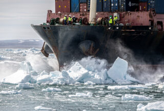 Container ship navigating through Arctic ice floes with crew monitoring deck operations, Bering Strait region
