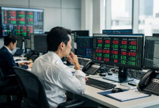Currency traders monitoring yen-dollar rates on screens in Tokyo dealing room, concerned expressions