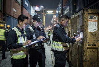 Customs officers inspecting shipping containers and export documents at Singapore port