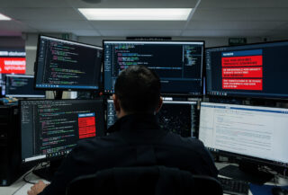 Cybersecurity analyst reviewing code alerts at Perth police cyber unit office, multiple monitors