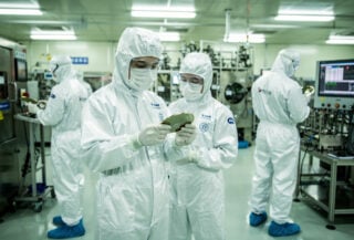 Engineers in cleanroom examining semiconductor wafers in Shanghai fab facility under bright industrial lighting
