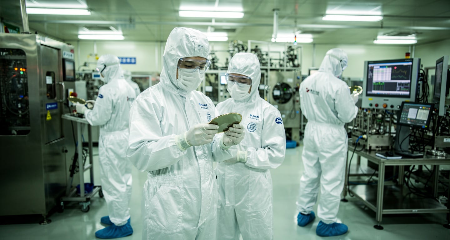 Engineers in cleanroom examining semiconductor wafers in Shanghai fab facility under bright industrial lighting