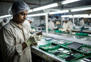 Factory worker examining smartphone on assembly line in Kanpur manufacturing facility, fluorescent lighting