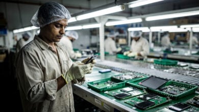 Factory worker examining smartphone on assembly line in Kanpur manufacturing facility, fluorescent lighting